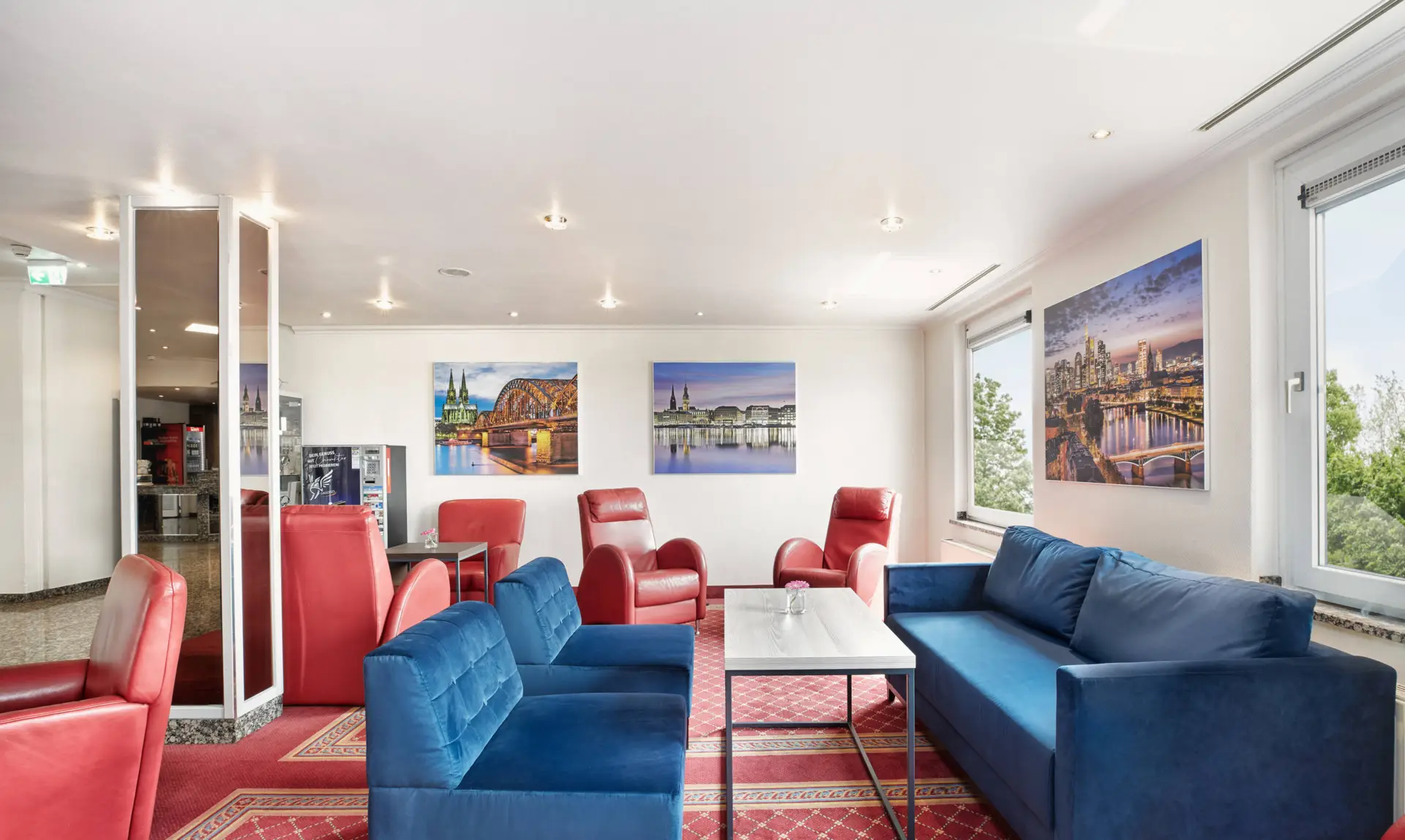 Lounge mit blauen Couchen und roten Sesseln. An der Wand hängen große Bilder.