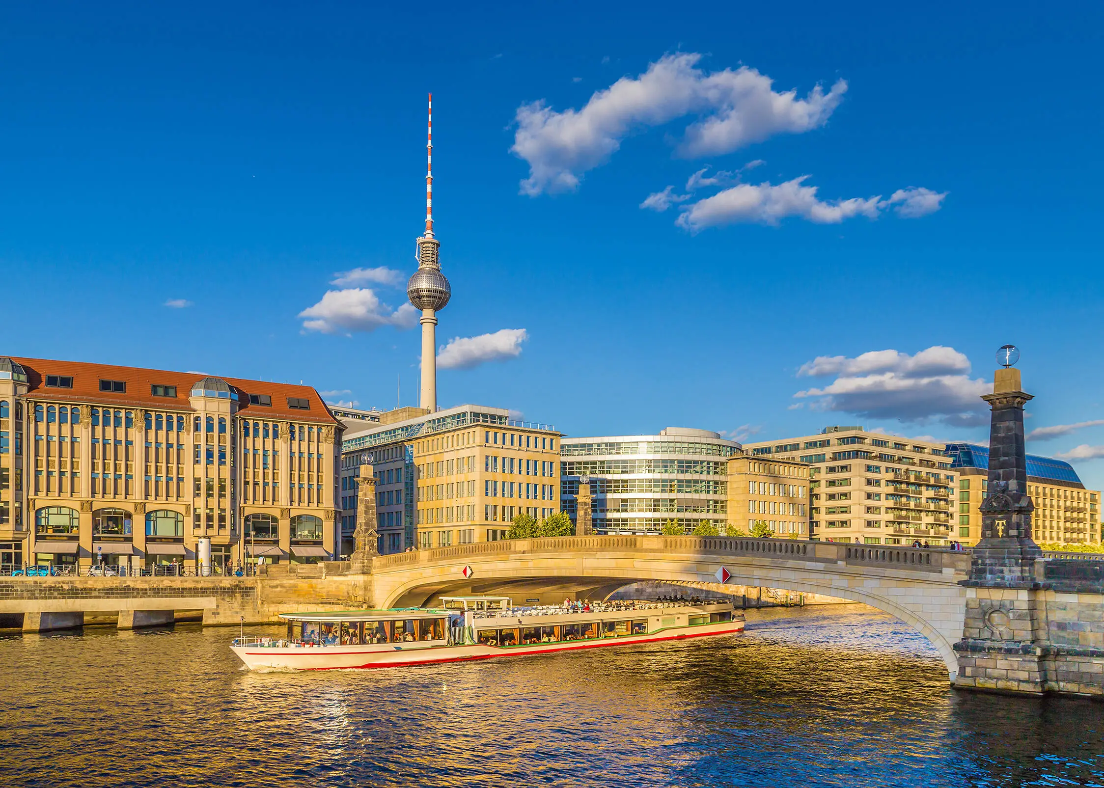 Blick über die Spree zum Berliner Fernsehturm. Auf der Spress fährt ein Ausflugsboot unter einer Brücke.
