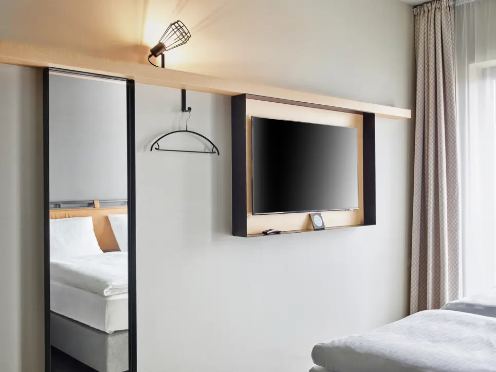 Fernseher und Spiegel an der Wand vor dem Bett.