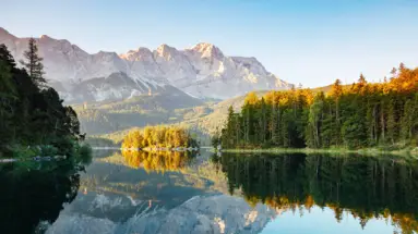 Montagne e una foresta di conifere vicino a un lago cristallino.