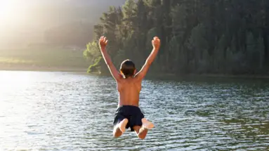 Ein Junge springt in einen See vom Steg aus.