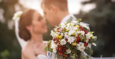 Im Vordergrund ein rotweißer Blumenstrauß. Im Hintergrund steht verschwommen ein Brautpaar.