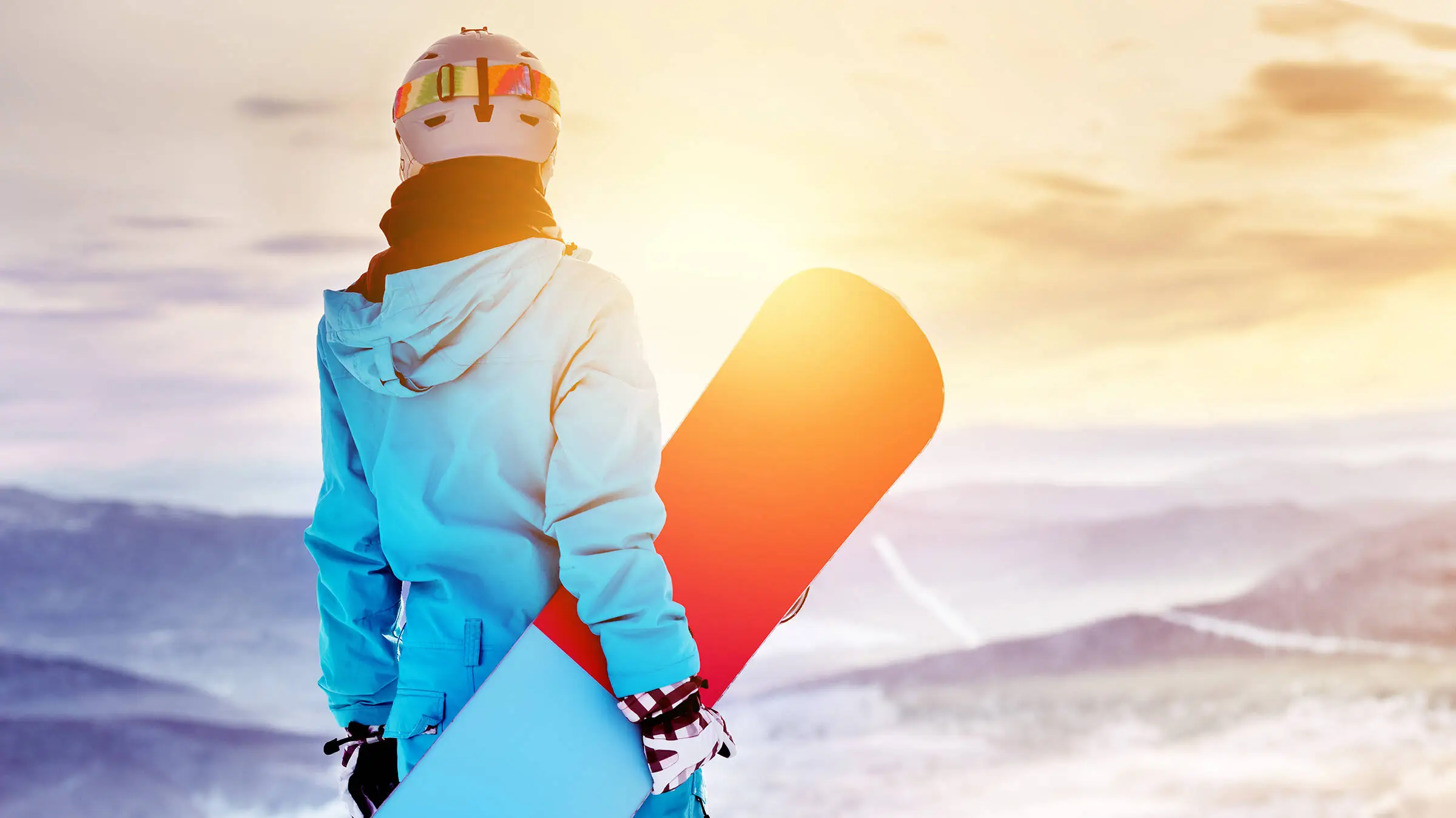 A snowboarder is standing with his snowboard in his hand.