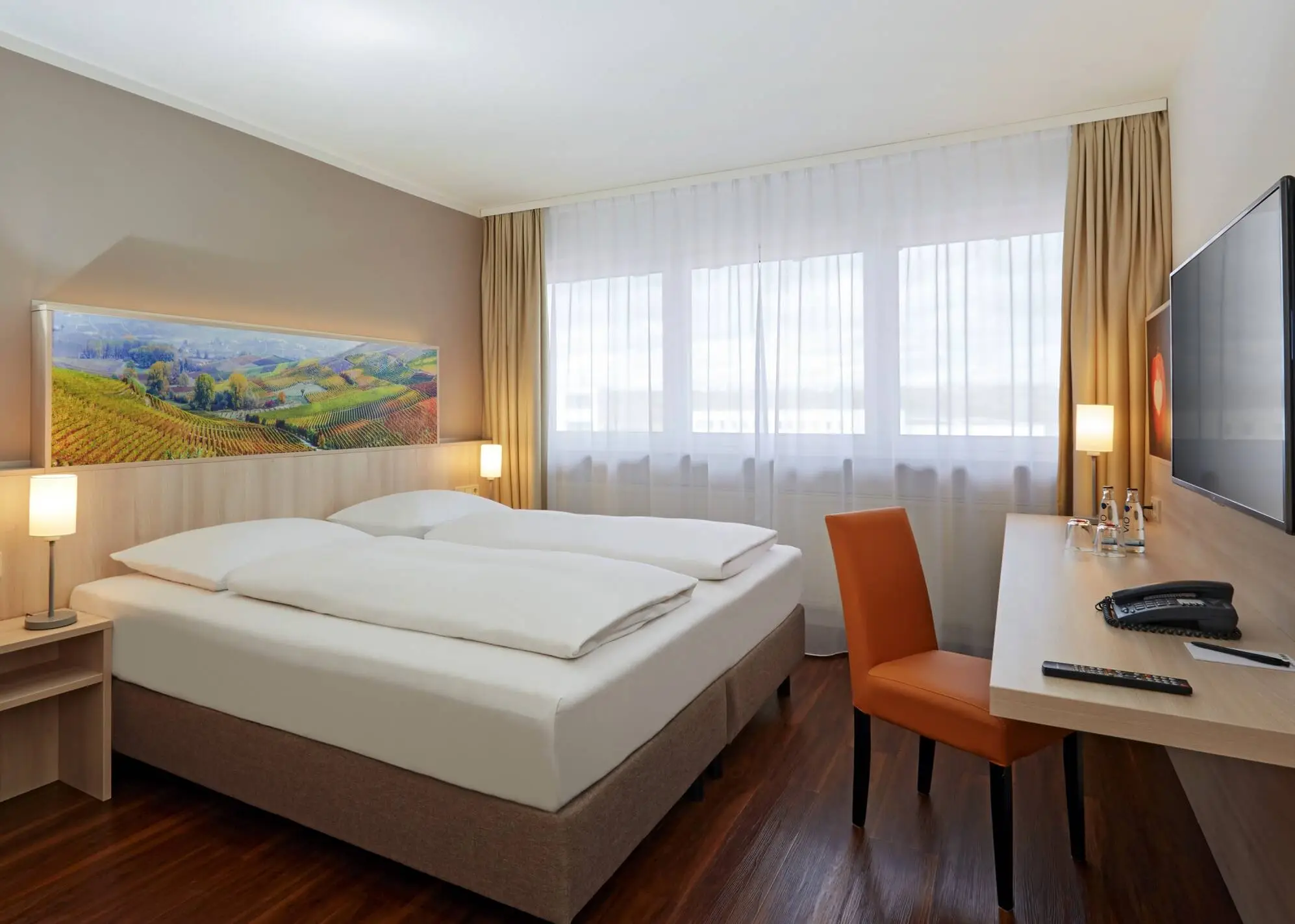 Hotel room with a large double bed. There is a desk in front of the bed.