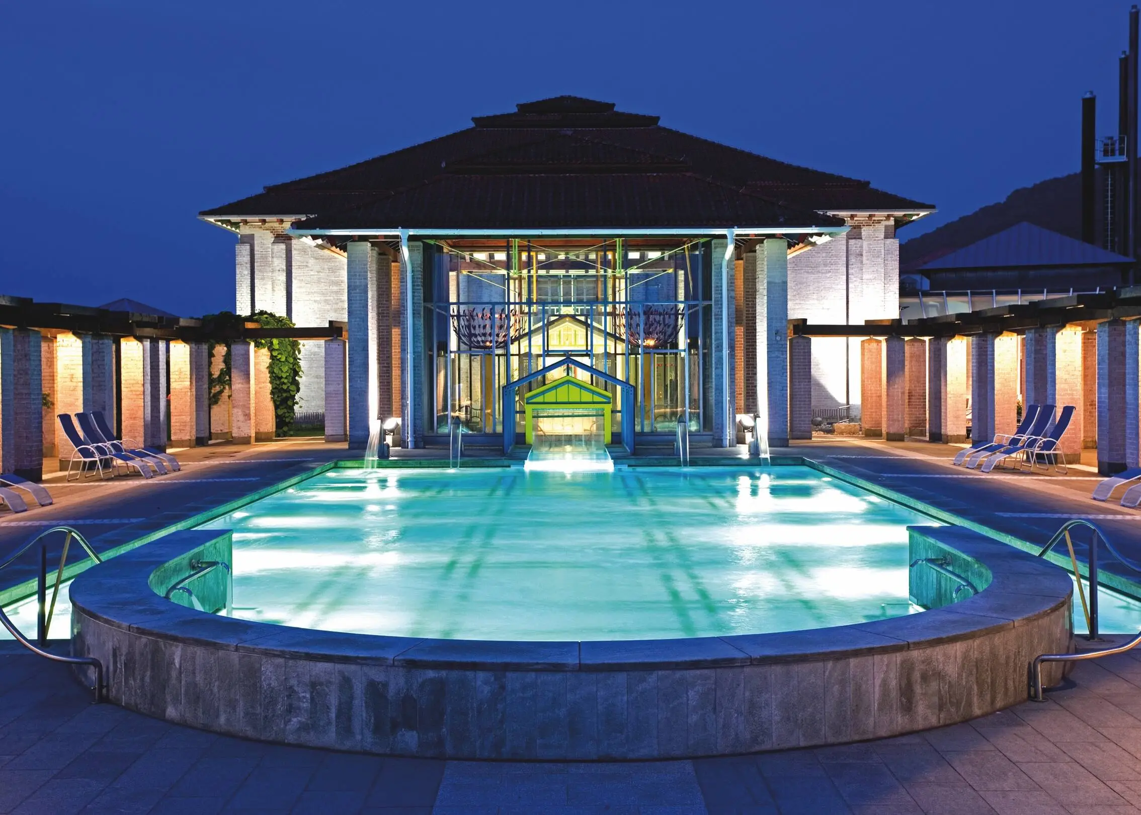 Beleuchteter Außenpool des Themalbads Limes-Thermen mit Liegen links und rechts auf der Terrasse neben dem Pool.