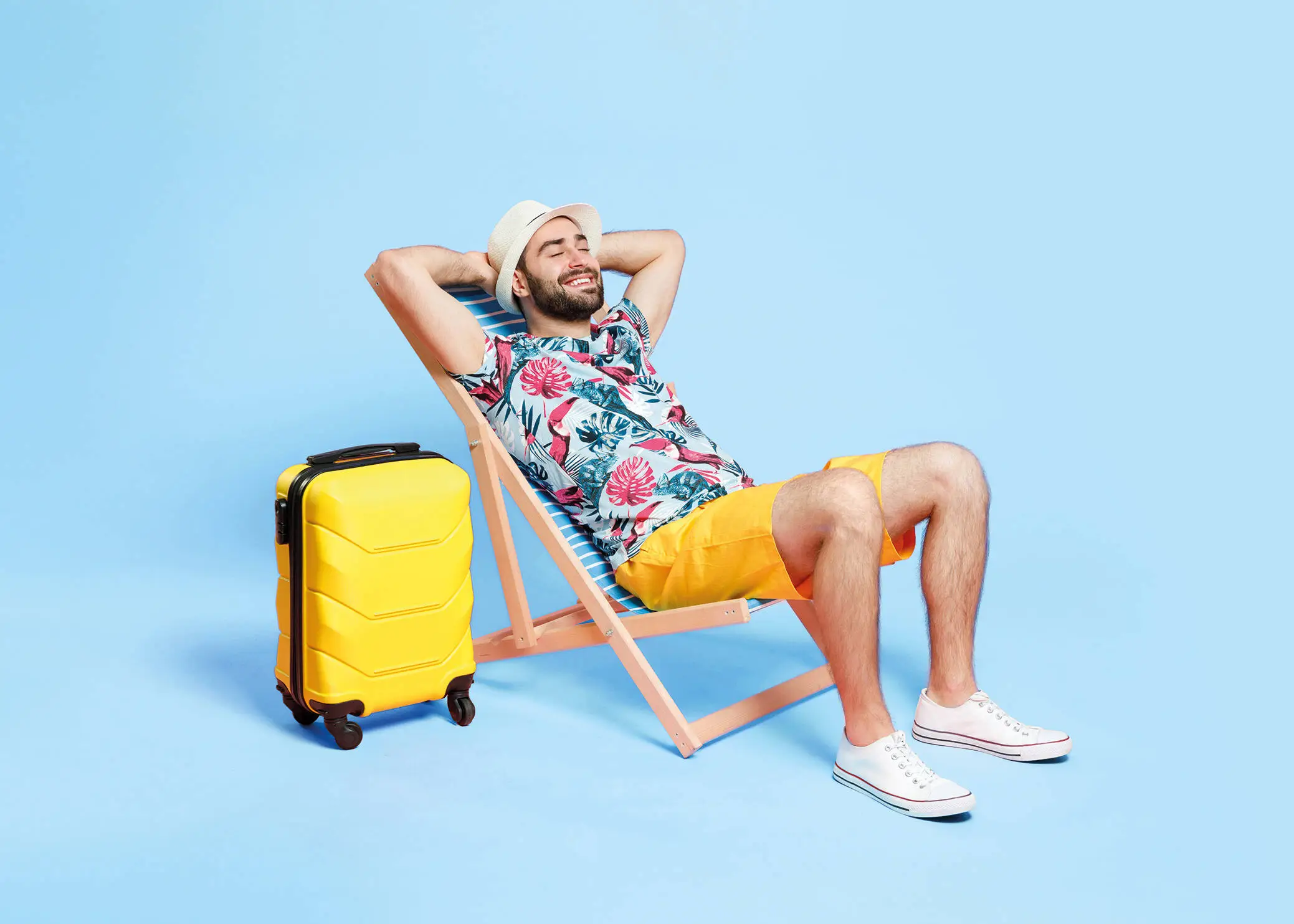Man in summer outfit lying on a deckchair in front of a blue background.
