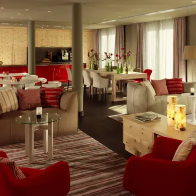 Große Lounge mit mehreren braunen Sofas und roten Stühlen. Im Raum stehen Holzmöbel und kleine Tische.