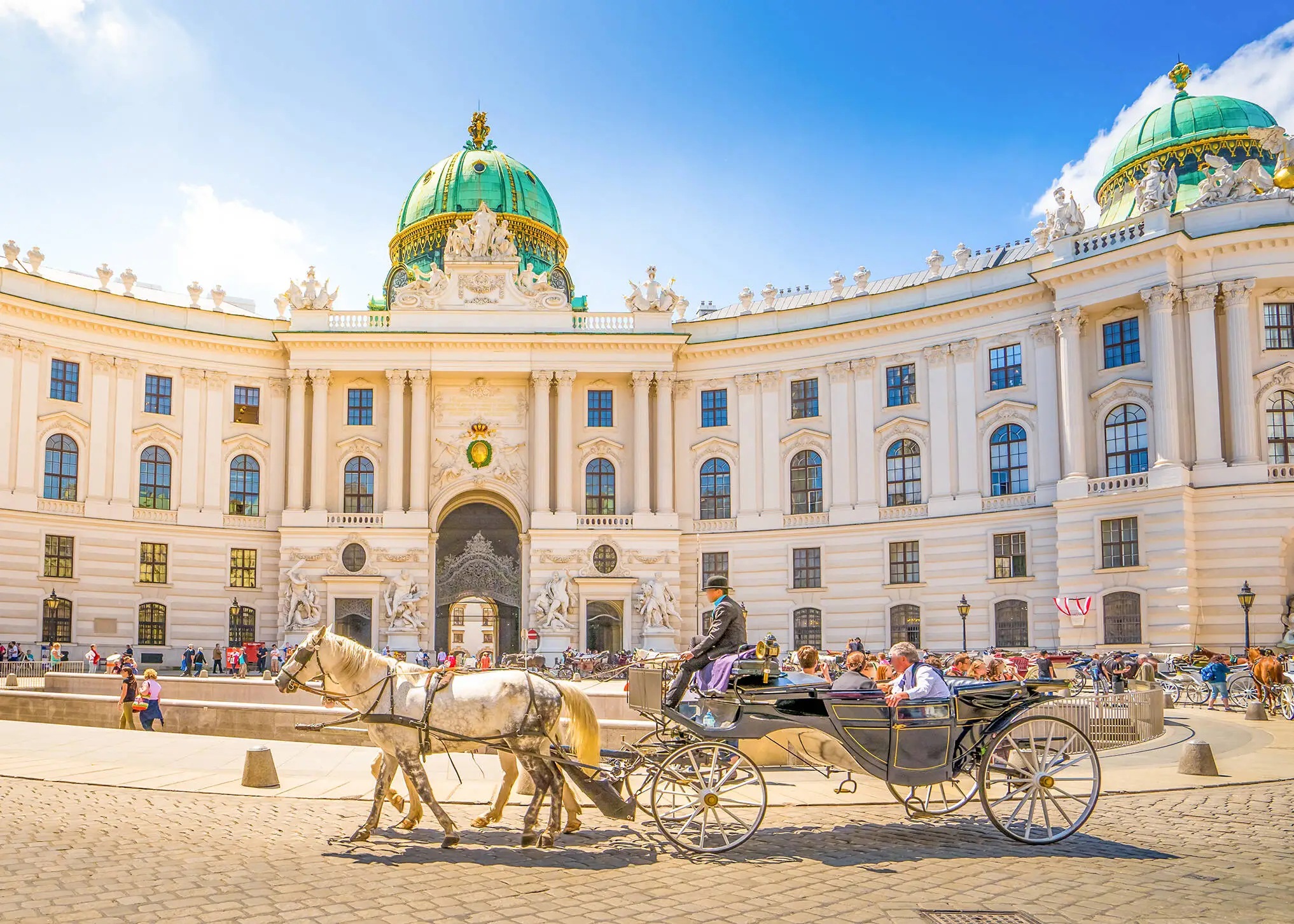 Blick auf die Hofburg in Wien im Sonnenschein mit Pferdekutsche im Vordergrund.