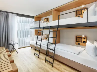 Vierbettzimmer mit Etagenbetten vor einem Fenster. 