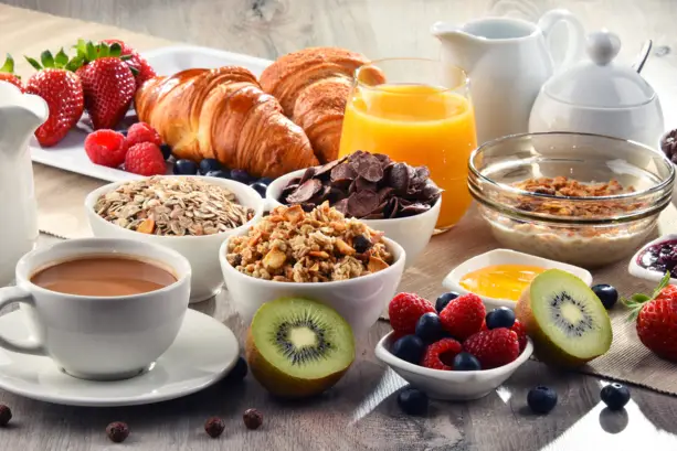 A breakfast table with croissants, muesli, fruit, juices and coffee.
