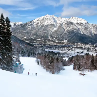 Winterlandschaft mit Blick auf dem weit entfernten Garmisch-Partenkirchen. Am Horizont sieht man das Gebirge.