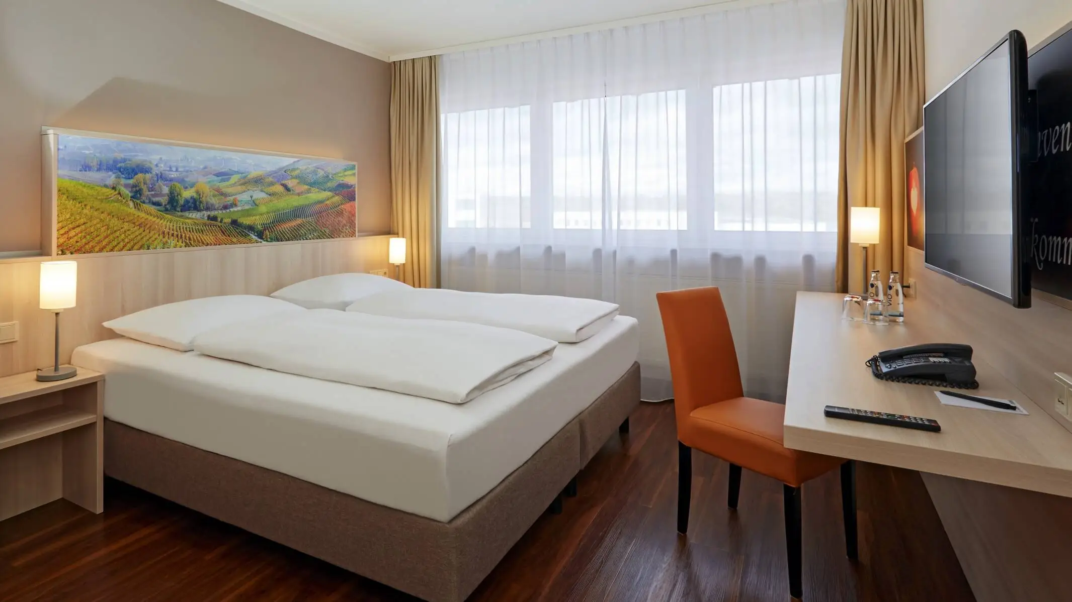 Hotel room with a large double bed. There is a desk in front of the bed.