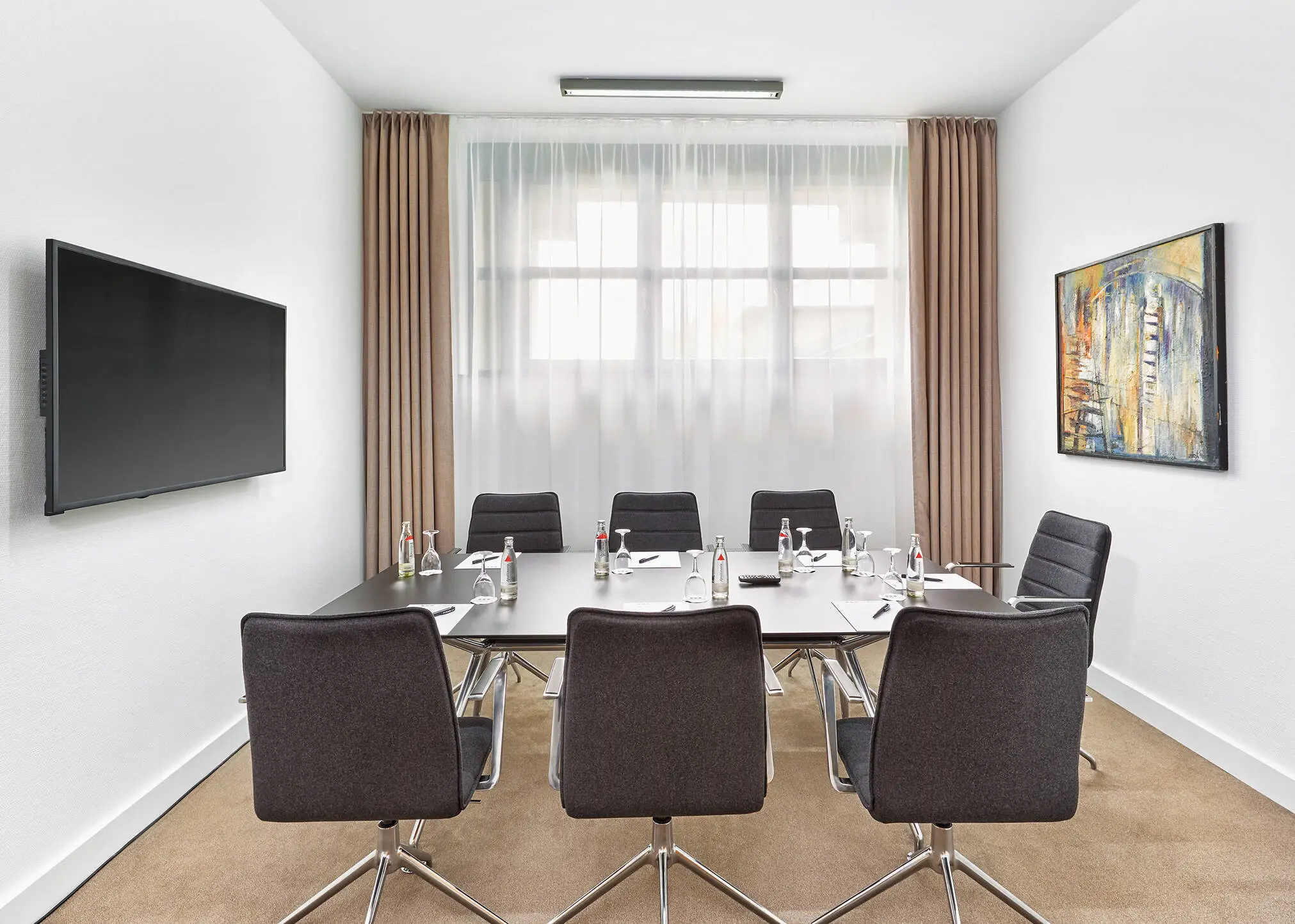 Kleiner Konferenzraum mit einem Konferenztisch. An der Wand hängt ein Fernseher.