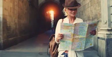 Eine Frau im frühlingshaften Outfit sthet vor einem Durchgang und schaut auf eine Stadtkarte.