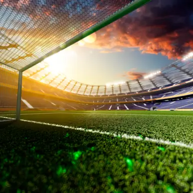 Dans un stade de football, vue sur la pelouse depuis les buts au coucher du soleil. Dans le ciel, on peut voir le soleil couchant et des nuages.