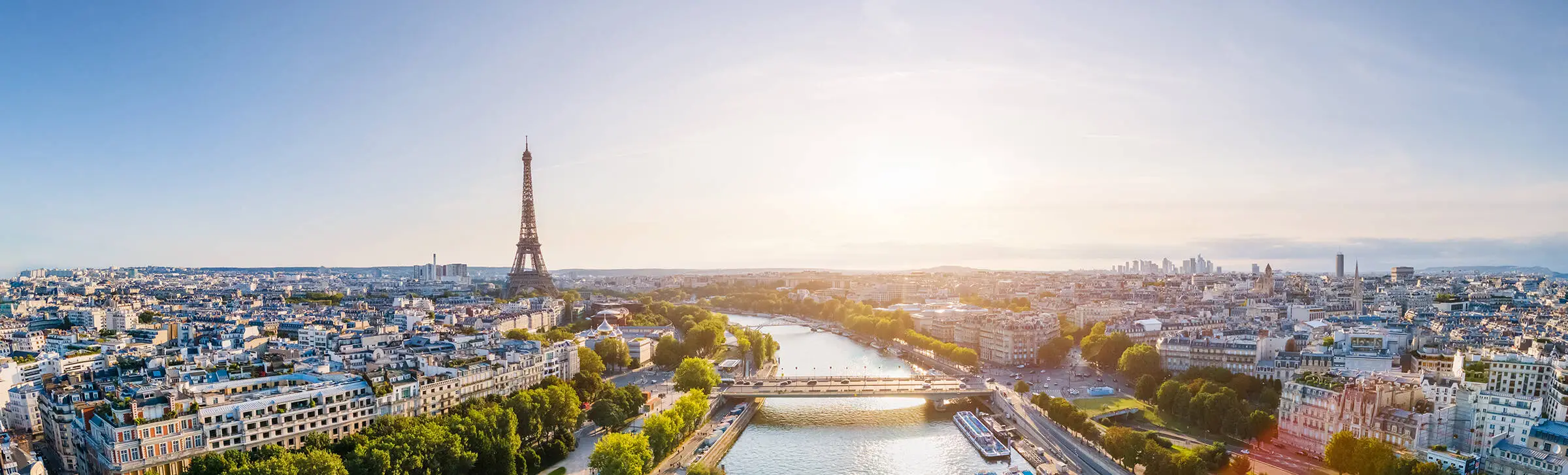 View over Paris with the Seine in the centre of the picture. To the left of the Seine in the background is the Eiffel Tower.