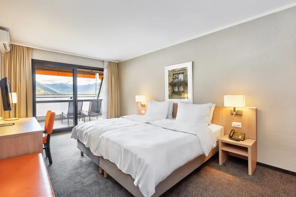 Helles Zimmer mit einem Doppelbett und einem Balkon.