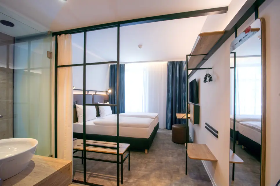 Hotelzimmer mit einem Doppelbett und einem offenen Badezimmer. Das Badezimemr ist mit einem Vorhang abtrennbar.