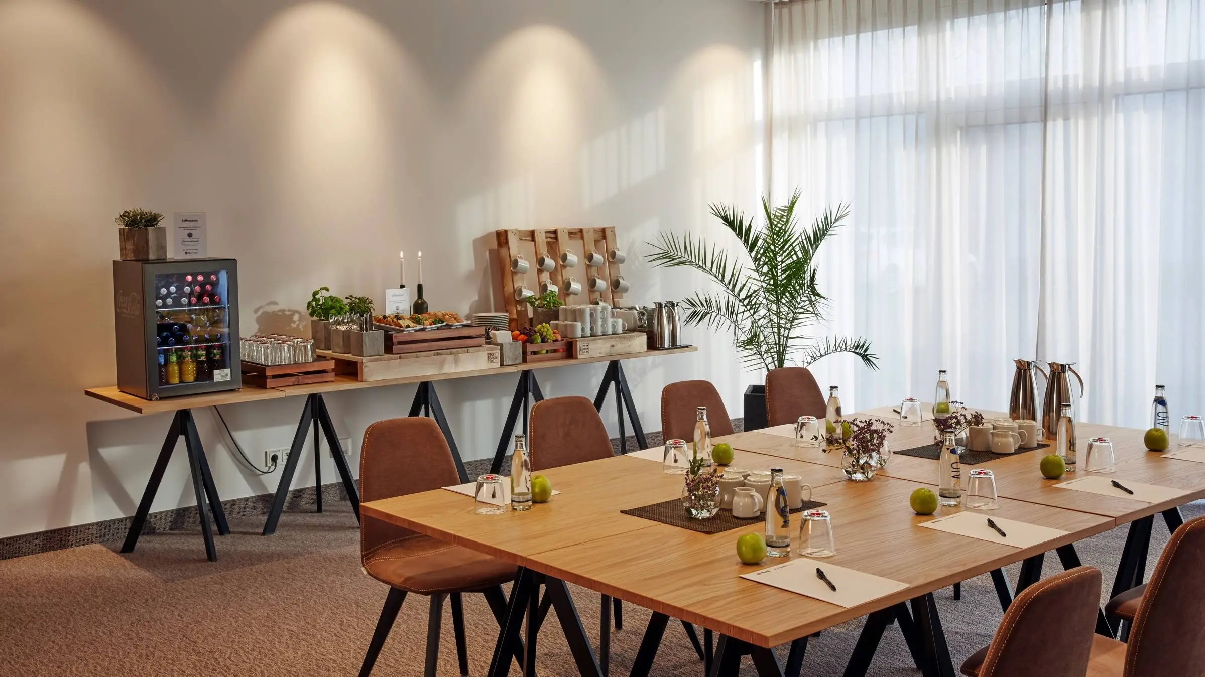 Aufenthaltsraum vom Tagungsbereich mit einem großen Esstisch. Dahinter ist ein kleiner Buffetttisch.