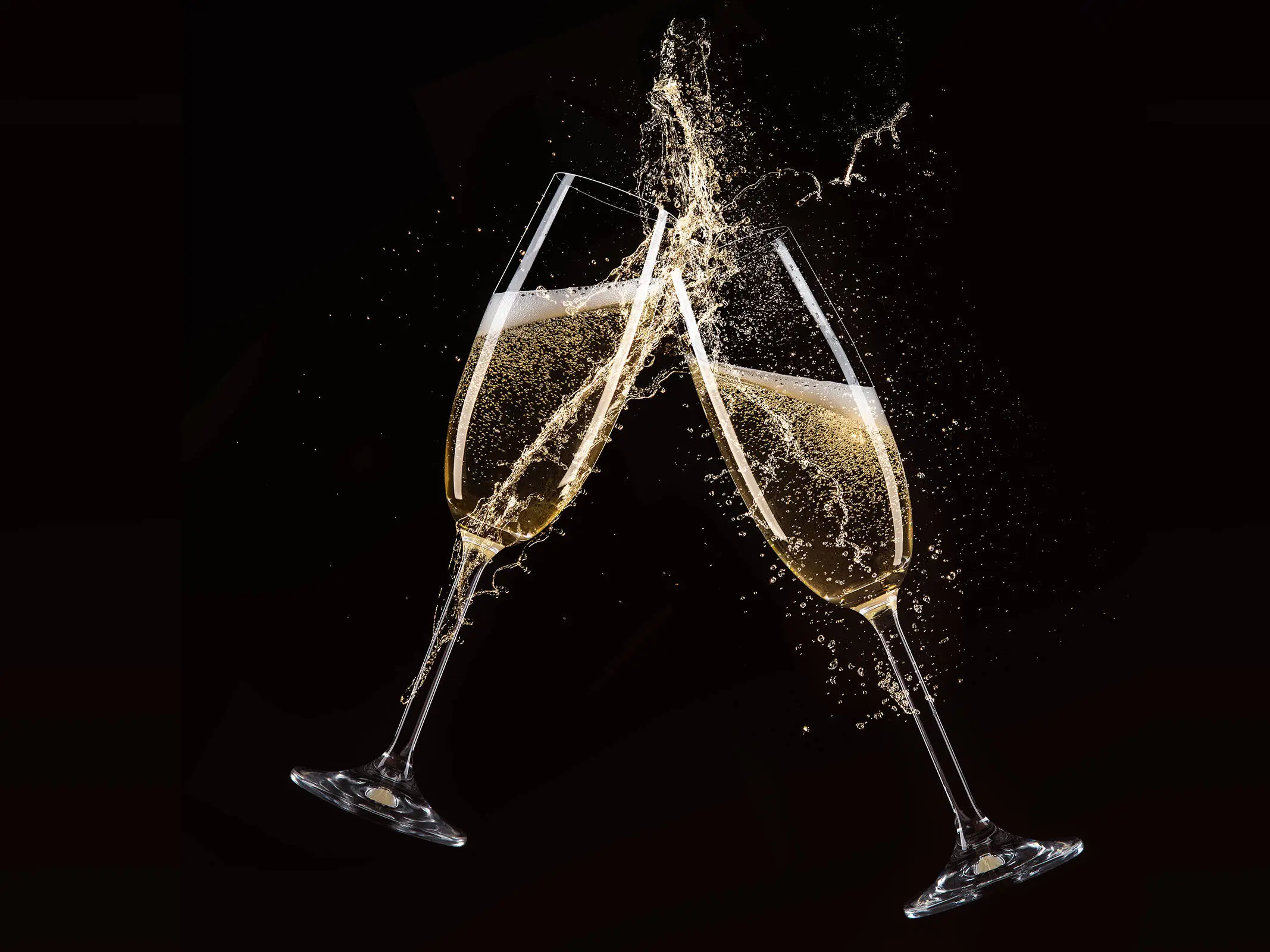 Zwei Sektgläser stoßen aneinander vor einem schwarzen Hintergrund.