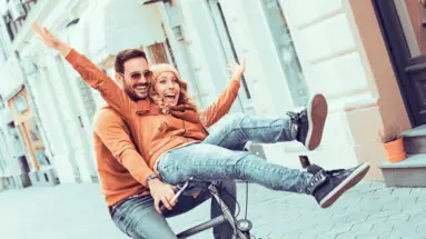 Man and woman riding a bicycle. The woman sits on the handlebars and is happy.
