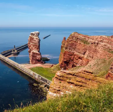 Rote Felssäule und Abseits eine Felswand am Meer auf Helgoland. Genannt wird diese Formation Lange Anna.