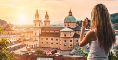 Eine Frau fotografiert den Sonnenuntergang in Salzburg. Im Hintergrund steht der Salzburger Dom.