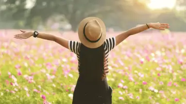 Frau steht im Blumenfeld und hebt die Arme Frau steht im Blumenfeld und hebt die Arme