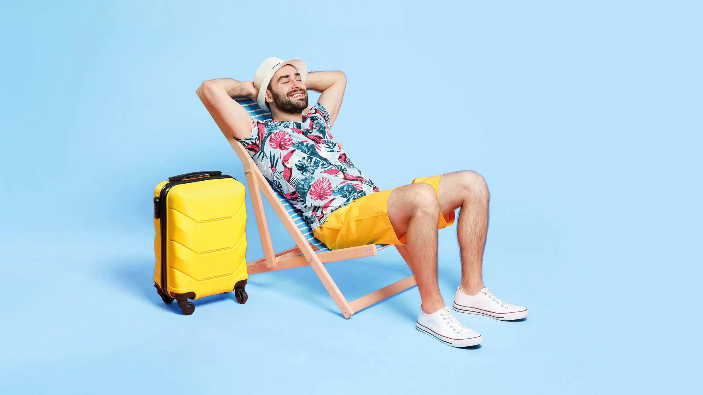 Mann im Sommeroutfit liegt auf einem Liegestuhl vor einem blauen Hintergrund. 