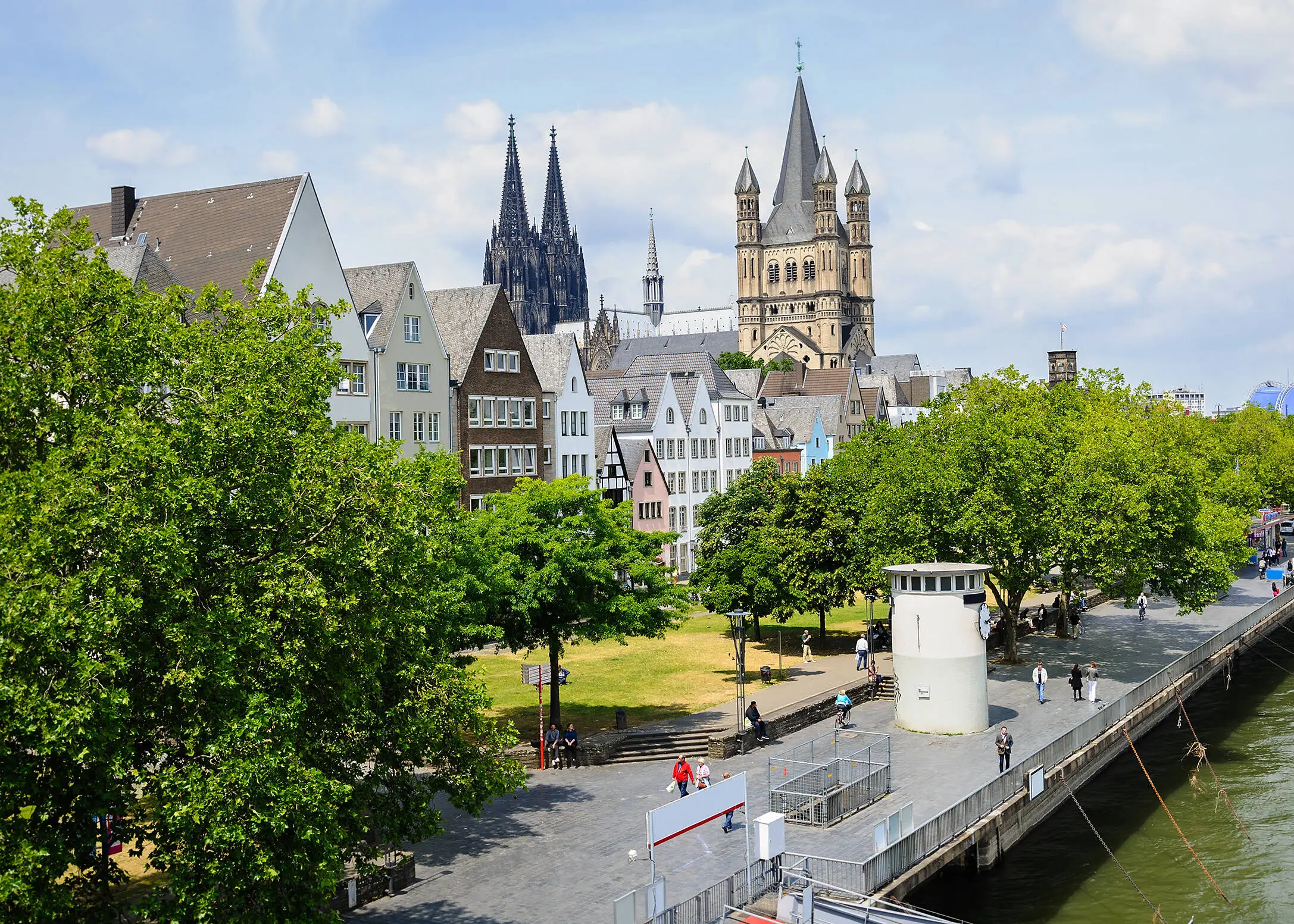 Blick auf die Altstadt und die Rheinuferpromenade in Köln von einer Rheinbrücke aus. Im Hintergrund befinden sich die Türme des Kölner Doms.