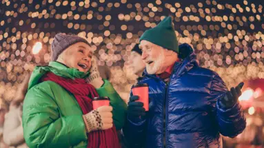 Ein älteres Paar trinkt Glühwein auf einem Weihnachtsmarkt.