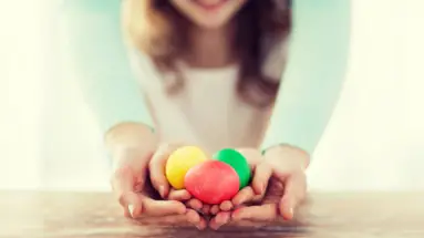 Eine Frau und ein Mädchen halten gemeinsam drei bunte Eier.