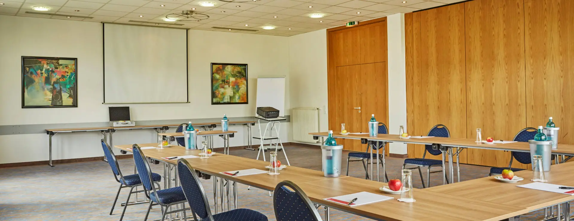 Seminarraum mit einer UForm-Bestuhlung. An der Wand hängt eine große Leinwand.