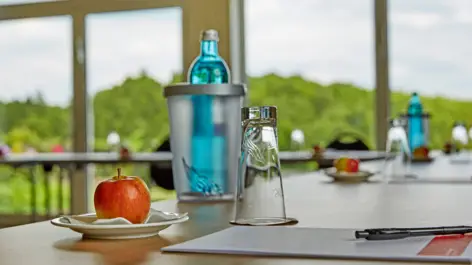 Nahaufnahme von einem Konferenztisch mit einem Apfel, eine Flasche Wasser und einem Schreibblock.