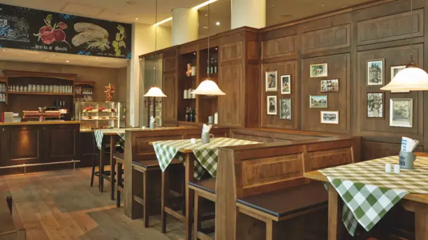 Restaurant mit Sitzplätzen vor großen Fenstern. An der Wand ist eine Fototapete von der Münchener Skyline.